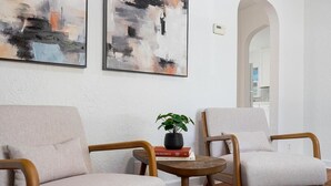 Una sala de estar moderna con dos sillones, una mesita redonda con una planta y libros, y arte abstracto en la pared.