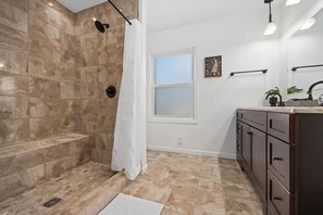 A bathroom with a shower, a sink, and a window.