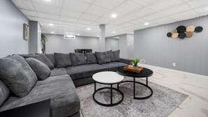 Una sala de estar moderna con un sofá seccional gris, una mesita redonda y una pequeña mesa auxiliar.