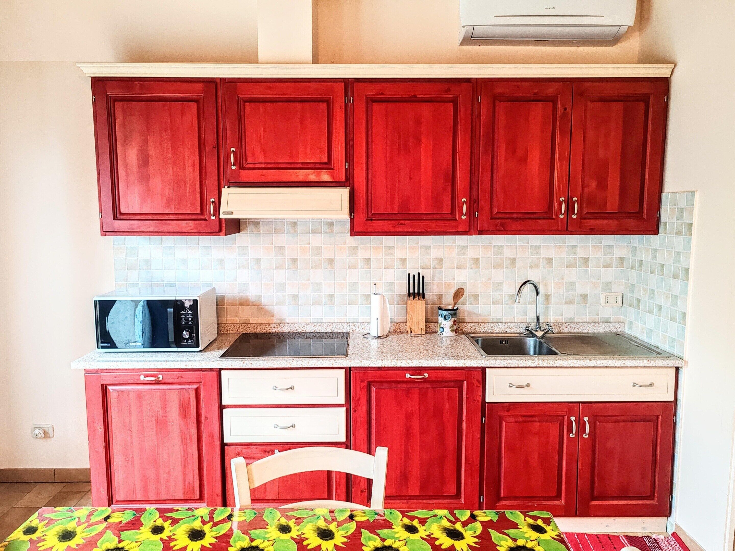 Una cucina compatta con pensili rossi, un forno a microonde, un lavandino e una sedia.