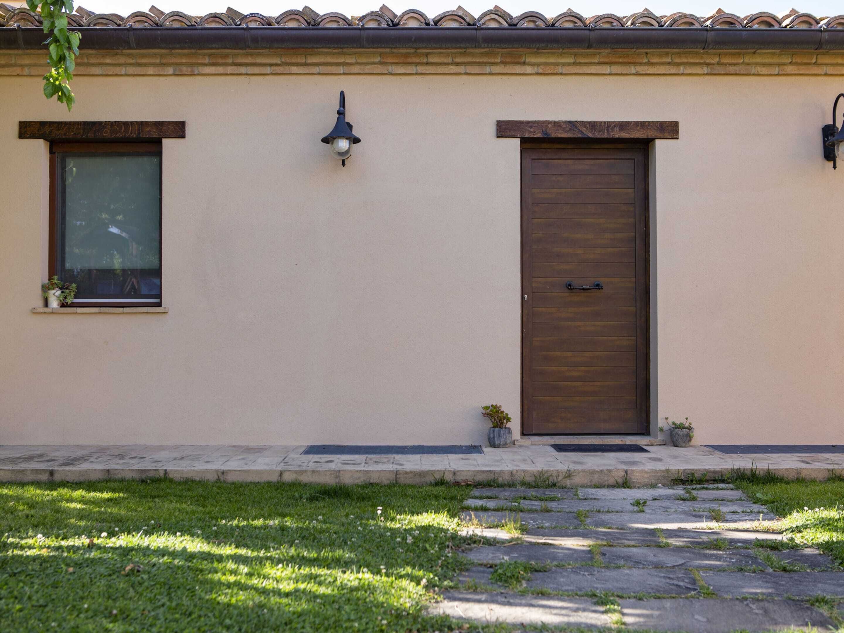 A building with a beige facade, a wooden door, and two windows with external lighting fixtures.