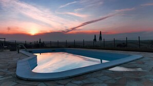 A swimming pool with a stone deck, surrounded by a fence and hills in the background. - Farmhouse in Marche With Pool & Wine Tours (Montecarotto)