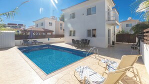 Ein Swimmingpool mit Liegestühlen und einem Tisch, umgeben von einem weißen Gebäude mit Balkonen.