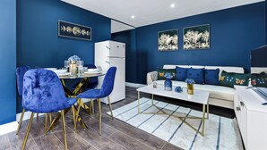 Un salon moderne avec un mur bleu, un canapé blanc, des fauteuils bleus et un coin repas comprenant une table et des chaises blanches.