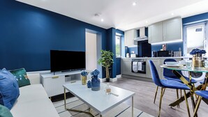 Un salon moderne doté d’un téléviseur à écran plat, d’une table basse en verre et d’un coin repas avec des chaises bleues et une table en verre.