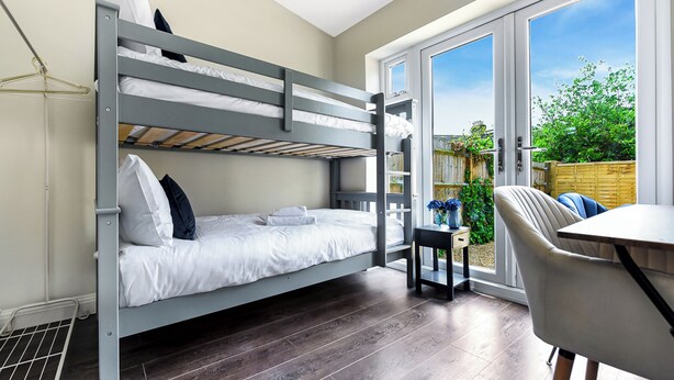 Une chambre avec un lit superposé, une table et une chaise, une fenêtre donnant sur un espace verdoyant et une porte menant à l’extérieur.