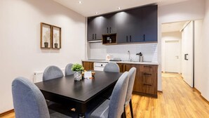 Une cuisine moderne avec des meubles de couleur sombre, un plan de travail blanc et une table à manger en bois, accompagnée de six chaises.