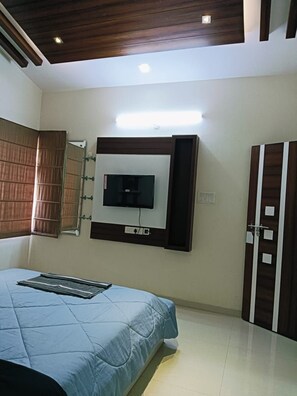 A bedroom with a bed, a TV mounted on the wall, a wardrobe, and a ceiling with wooden beams. - Corporate guest house (Medchal)