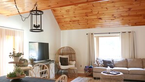 Un salon chaleureux avec un plafond en bois, une télévision, un canapé et un coin repas comprenant des chaises et une table.