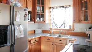 Une cuisine avec des meubles de rangement en bois, un réfrigérateur, un évier et une fenêtre avec des rideaux.
