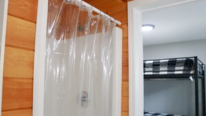 Une pièce avec un mur en bois, un rideau de douche et un lit superposé recouvert d’une couverture à carreaux.