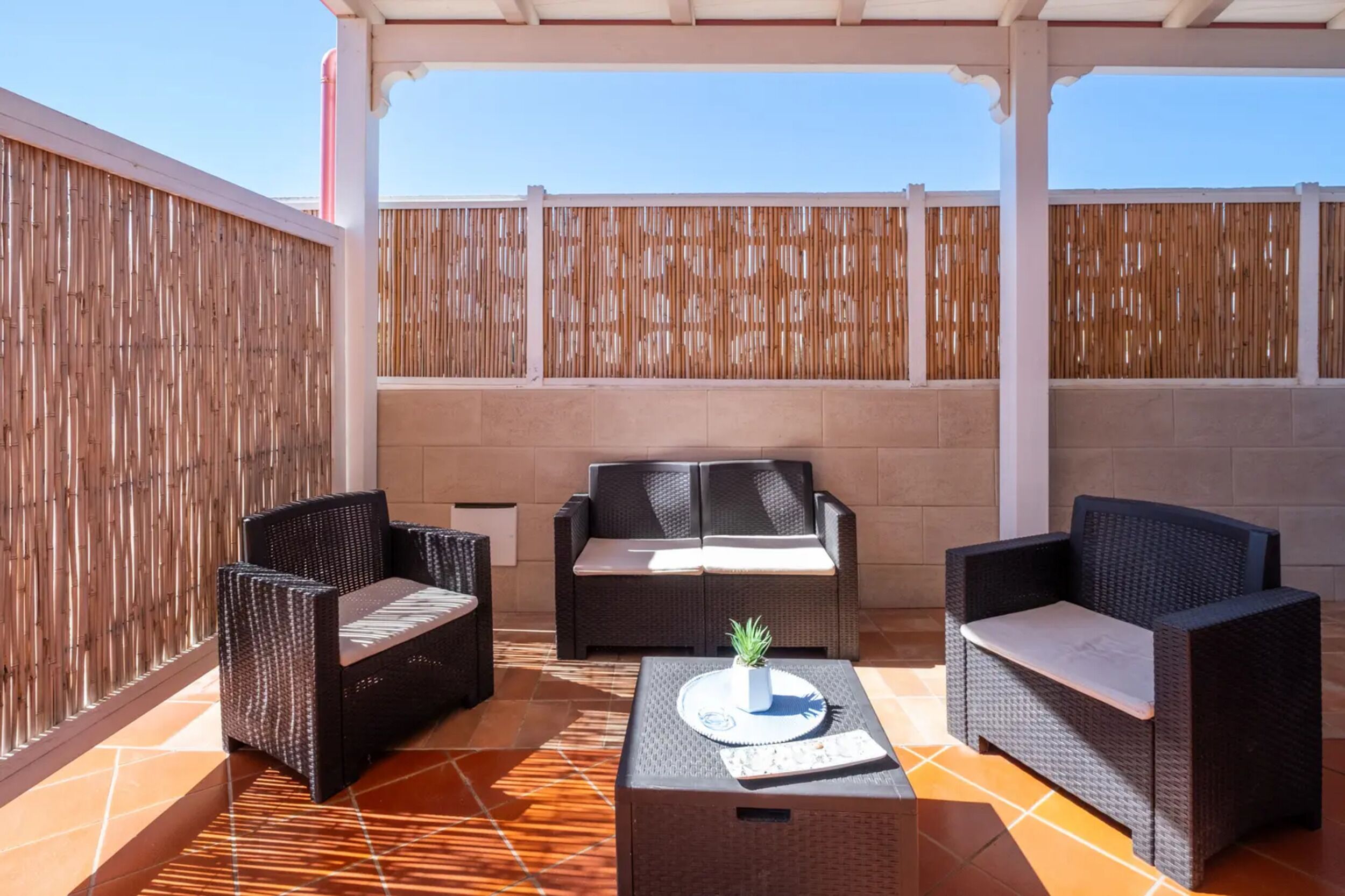 An outdoor patio area with wicker furniture, a small table with a plant, and a tiled floor.