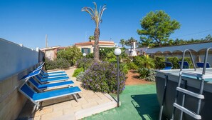 Un espace piscine avec des chaises longues, un palmier et un ciel d’un bleu limpide.