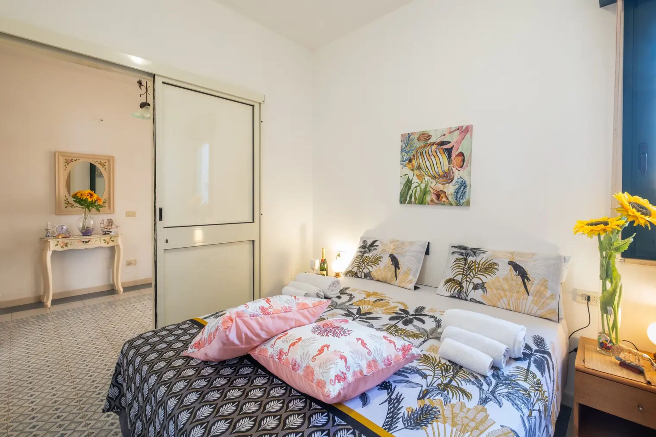 Une chambre à coucher avec un lit, des oreillers, une table de chevet, un vase de fleurs, un tableau et une armoire.