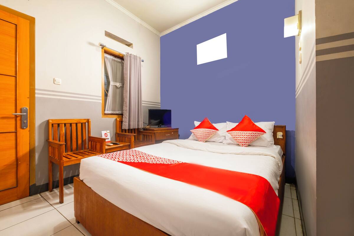 Ett hotellrum med en säng, en trästol, ett skrivbord med en dator och ett fönster med gardiner.
