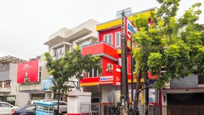 Une vue de rue avec un chariot de vente de nourriture bleu, un bâtiment rouge et jaune, et un arbre au premier plan.