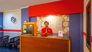 Un espace d’accueil d’hôtel avec un comptoir en bois, un mur rouge et des carreaux décoratifs.