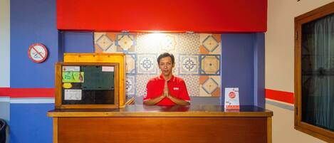 A hotel reception desk with a person in a red uniform standing behind it.