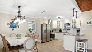 A modern kitchen with a central island, stainless steel appliances, and a dining area with a marble table and wooden chairs. - 3BR Marco Island home with heated pool, WiFi and full kitchen. (Marco Island)