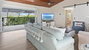 A spacious living room with a large sofa, a television, and a balcony with a view of greenery. - 3BR Marco Island home with heated pool, WiFi and full kitchen. (Marco Island)