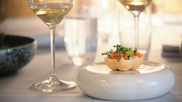 A dining table with a white plate holding a small appetizer, two wine glasses, and a bowl in the background.