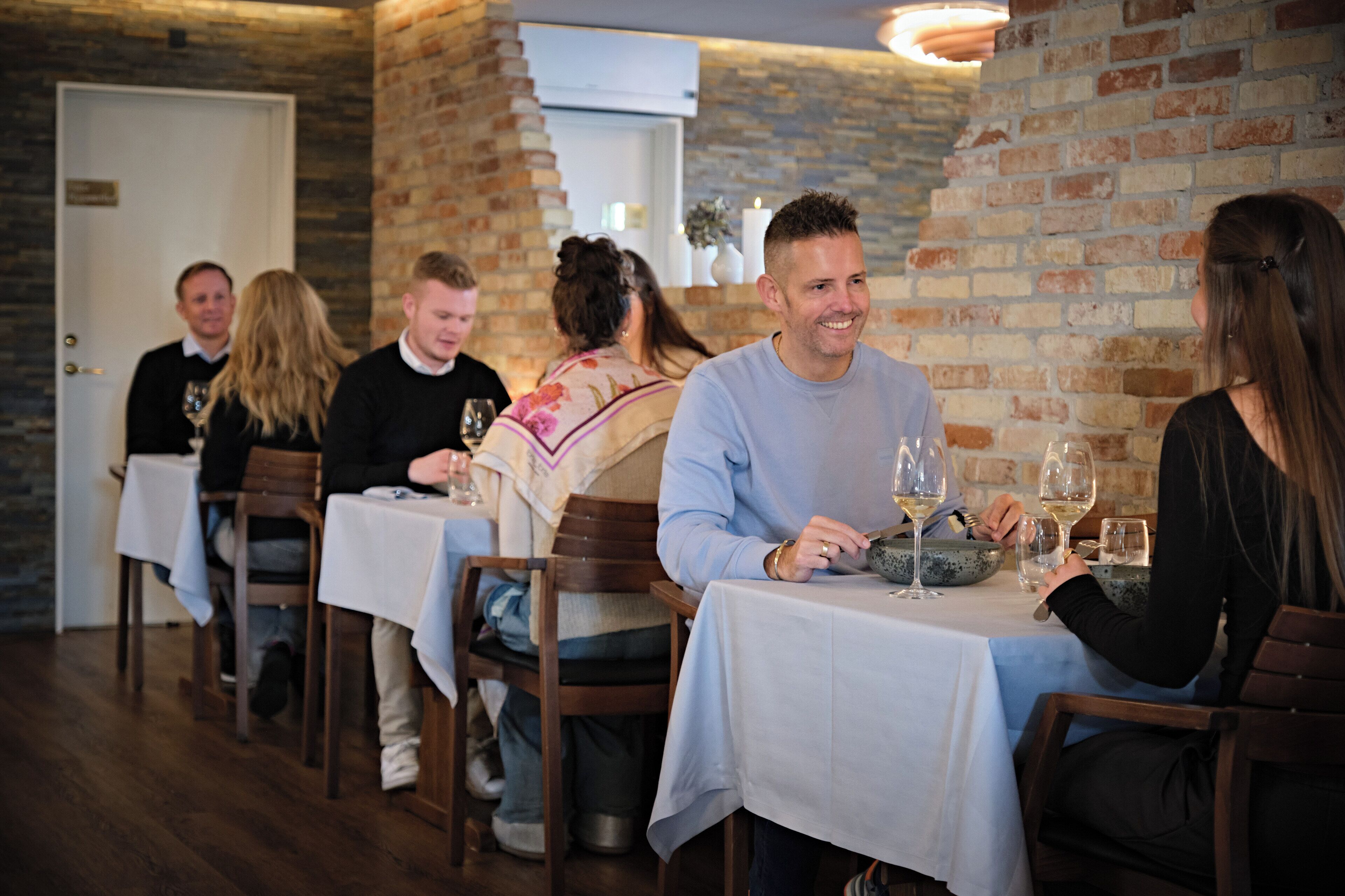 Un restaurant aux murs de briques et aux tables en bois, chacune recouverte d’une nappe blanche.
