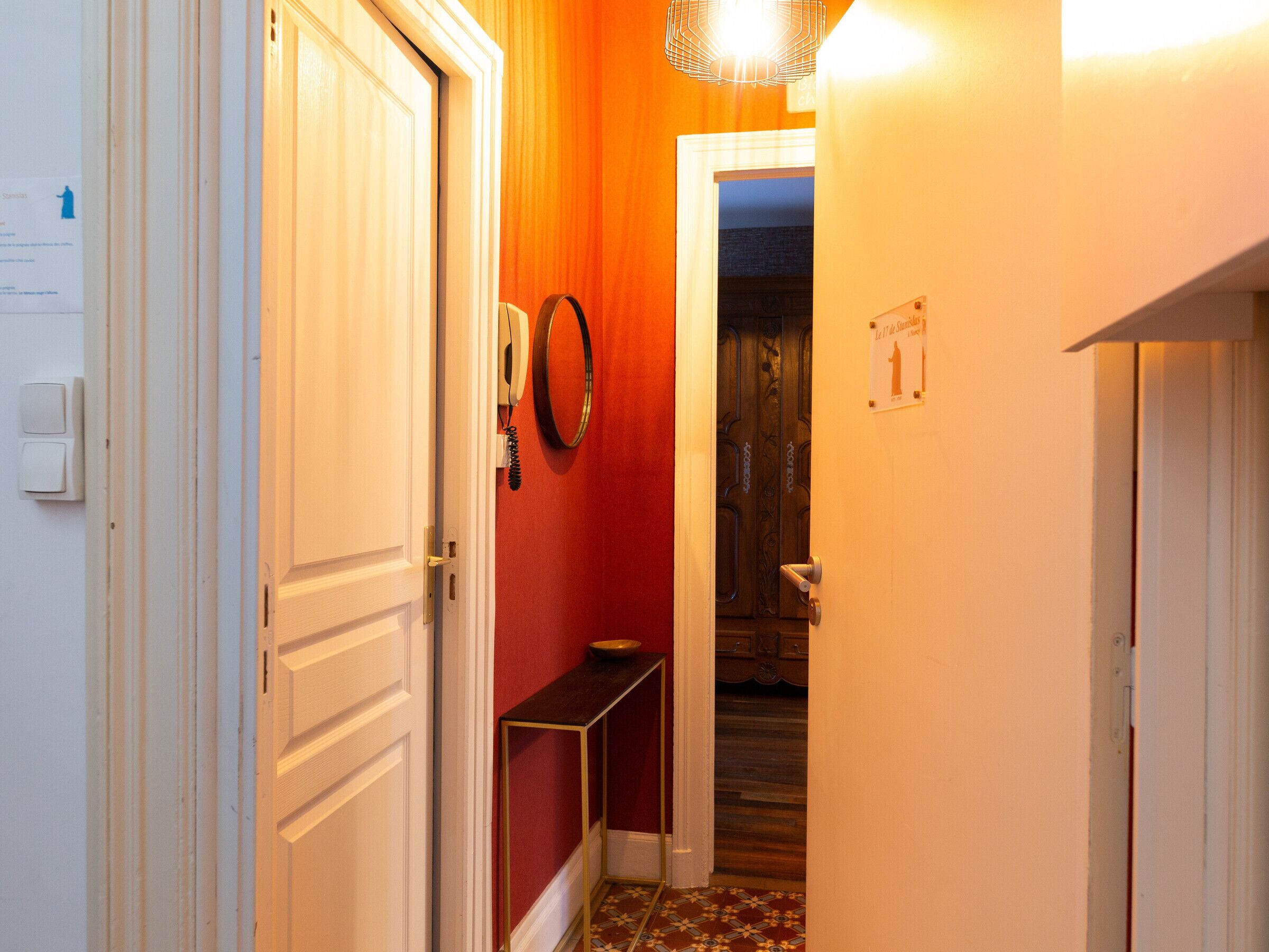 Een gang met een witte deur, een rode muur, een klein tafeltje en een lamp.