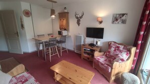 Un salon chaleureux avec une table basse en bois, un canapé à motifs, une table à manger avec des chaises, un téléviseur et une lampe fixée au mur.