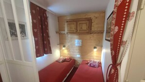 Une petite chambre accueillante, dotée de deux lits simples, de murs en bois et d’un aménagement simple et fonctionnel.