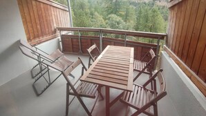 Un balcon avec une table et des chaises en bois, offrant une vue sur une vallée boisée.