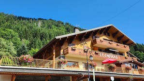 Eine Holzhütte mit Balkon, einem Schild mit der Aufschrift "UE CHOVAS" und einer Bergkulisse.