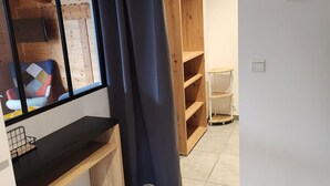 Ein Zimmer mit Holzboden, einem schwarzen Konsolentisch, einem großen Fenster mit Blick auf einen farbenfrohen Sessel und einer Holzhängeregalschrank.