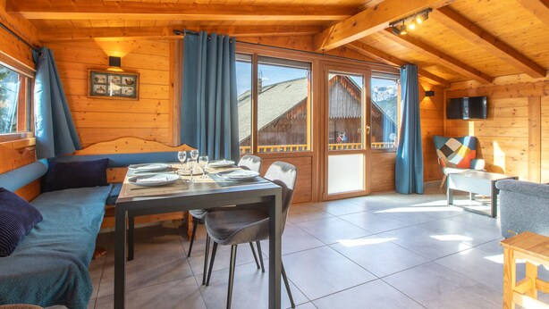 Ein gemütliches Holzhaus-Interieur mit Essbereich, einer Couch und einem an der Wand befestigten Fernseher.