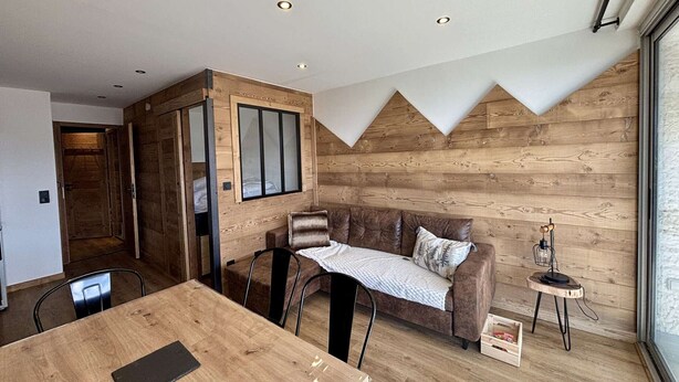 Una habitación acogedora con un revestimiento de madera, un sofá de cuero marrón, una mesa de comedor de madera y una mesita auxiliar con lámpara.