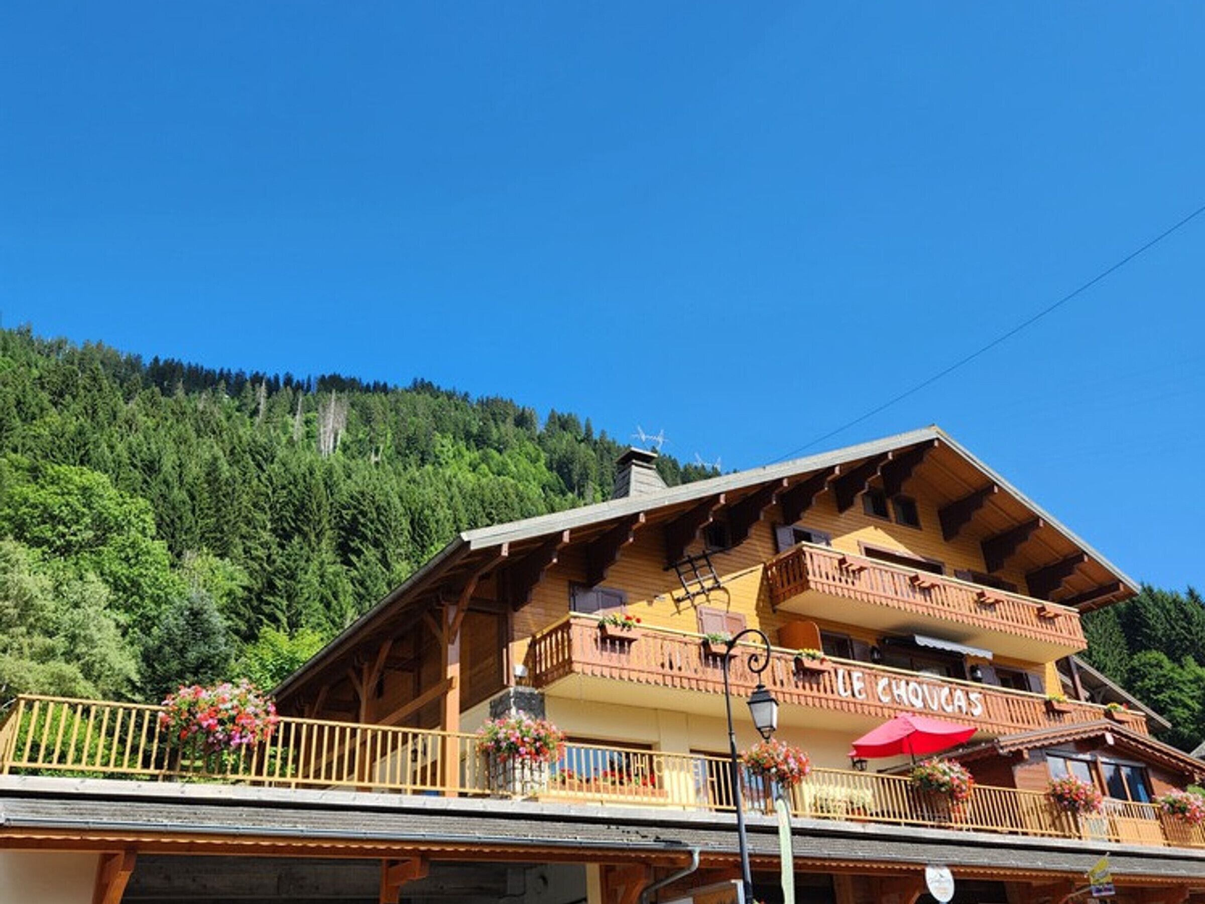 A wooden chalet with a balcony, a sign reading "UE CHOVAS", and a mountainous backdrop.