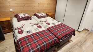 A bedroom with two beds, wooden walls, a painting, and a wardrobe. - 3-Room Chalet in Châtel, 6 Pers, South Balcony (Châtel)