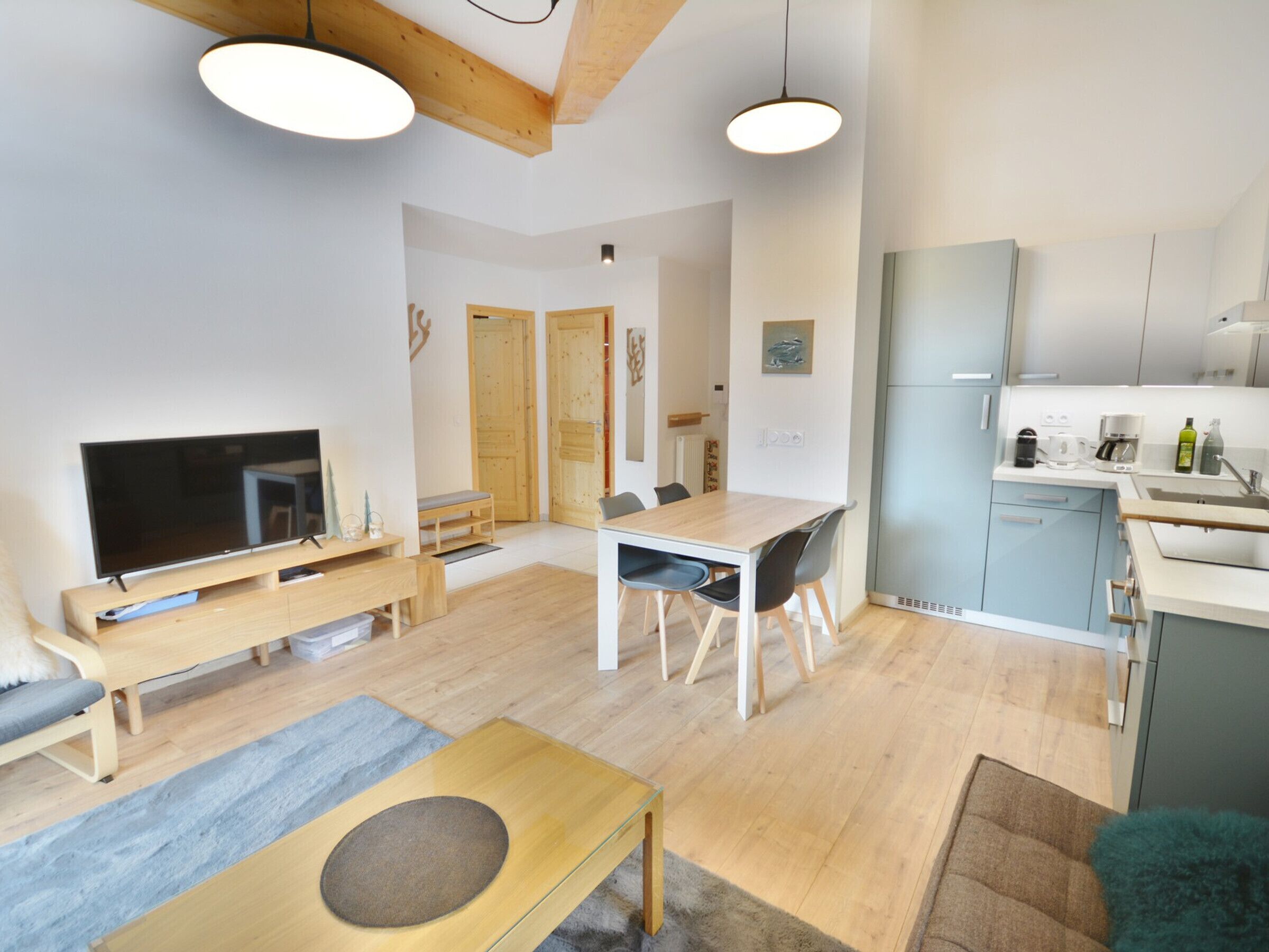 A modern living room with a flat-screen TV, wooden furniture, and a dining area with a table and chairs.