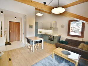 A modern kitchen with light blue cabinets, a wooden dining table with chairs, a brown sofa with a fur throw, and a window with a snowy view.