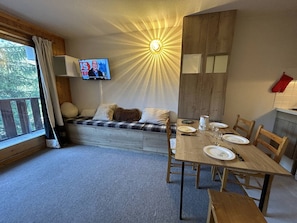 A cozy room with a wooden bench, a dining table set for four, and a television mounted on the wall.