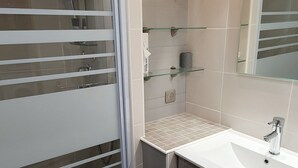 Een moderne badkamer met een douchecabine van glas, een wit wastafeltje en een glazen schapunit.