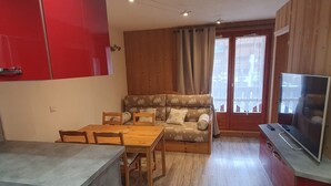 Een ruimtelijk ingerichte leefruimte met een eethoek, een bank, een televisie en een kitchenette.