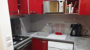 Een compacte keuken met een gasfornuis, een spoelbak, een magnetron en een vaatwasser.