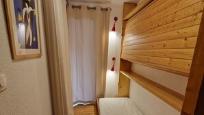 A narrow hallway with a wooden bunk bed, a white curtain, and a framed picture on the wall.