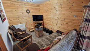 Un accogliente soggiorno con pareti in legno, una televisione a schermo piatto, un divano e una poltrona.