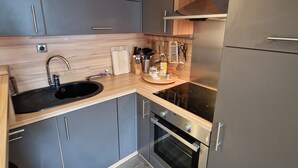 Una cucina moderna con mobili grigi, un lavello nero, elettrodomestici in acciaio inossidabile e piani in legno.