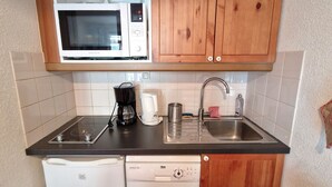 Una cocina compacta equipada con microondas, cafetera, lavaplatos y fregadero.
