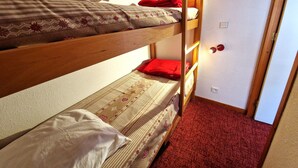 Habitación con literas, alfombra roja y una lámpara fijada a la pared.