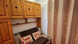 Habitación compacta con sofá cama, muebles de madera y cortina estampada con corazones.