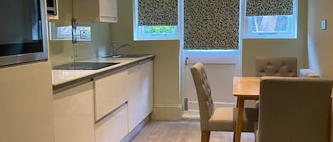 Une cuisine moderne avec des meubles blancs, un four encastré et un coin repas comprenant une table en bois et deux chaises.