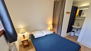 Une chambre à coucher comprenant un lit, une table de chevet, une lampe, ainsi qu’une salle de bain avec un lavabo et un miroir.